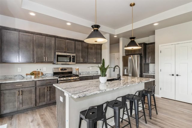 kitchen featuring light stone countertops, an island with sink, appliances with stainless steel finishes, and decorative light fixtures