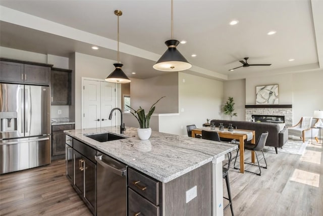 kitchen featuring sink, appliances with stainless steel finishes, an island with sink, pendant lighting, and a fireplace