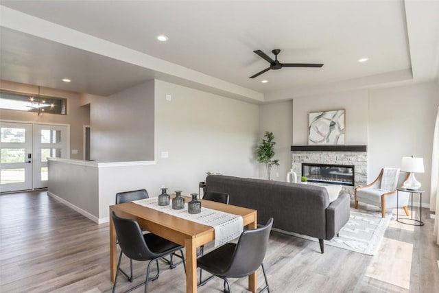 dining space featuring a stone fireplace, light hardwood / wood-style flooring, french doors, and ceiling fan