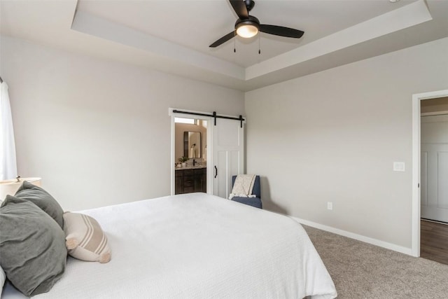 bedroom with ensuite bathroom, a tray ceiling, carpet floors, ceiling fan, and a barn door