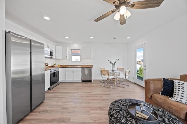 kitchen with appliances with stainless steel finishes, butcher block counters, white cabinets, ceiling fan, and light hardwood / wood-style floors