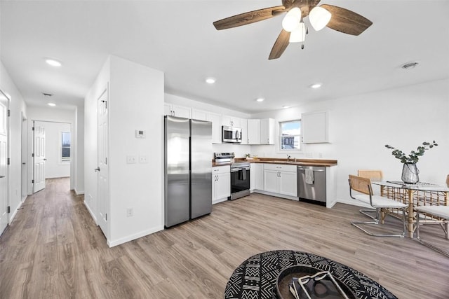 kitchen with sink, light hardwood / wood-style flooring, wooden counters, appliances with stainless steel finishes, and white cabinets