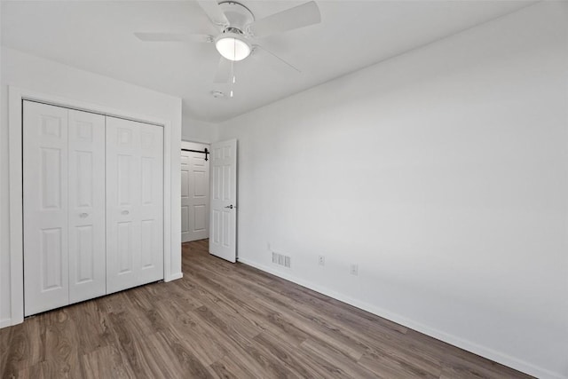 unfurnished bedroom with light hardwood / wood-style floors, a closet, ceiling fan, and a barn door