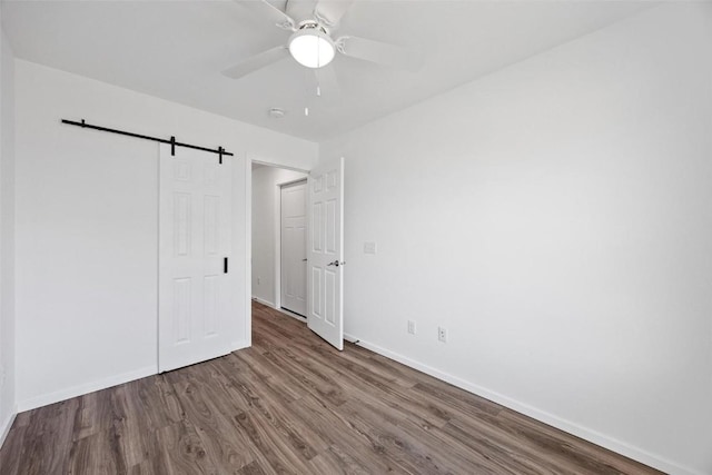 unfurnished bedroom with wood-type flooring, a barn door, and ceiling fan