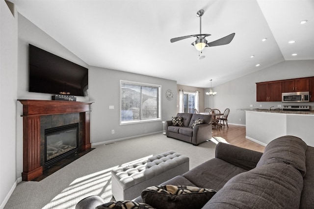 living room featuring vaulted ceiling, ceiling fan with notable chandelier, light colored carpet, and a fireplace