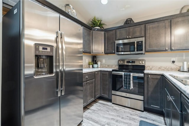 kitchen featuring vaulted ceiling, sink, light hardwood / wood-style floors, stainless steel appliances, and dark brown cabinets