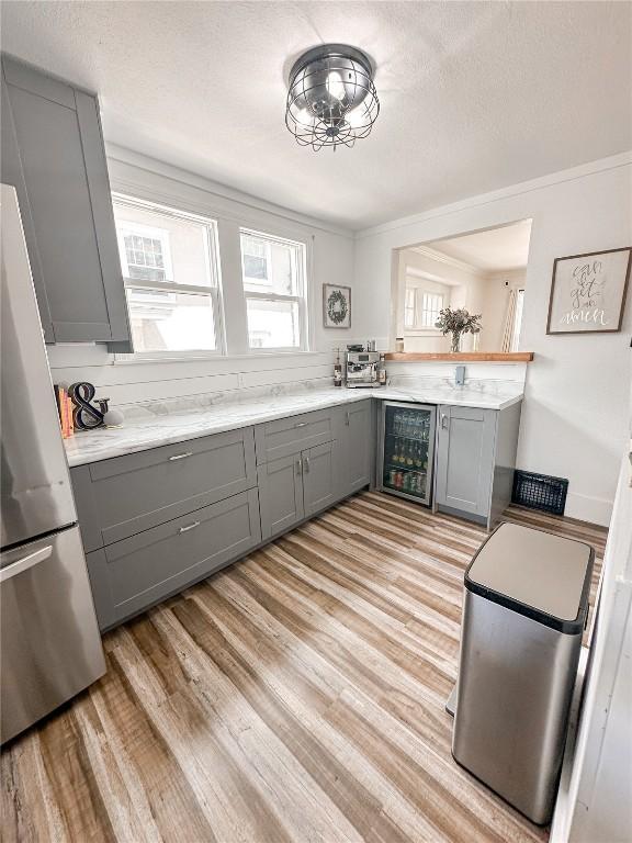 kitchen featuring gray cabinetry, wine cooler, stainless steel fridge, crown molding, and light wood-type flooring