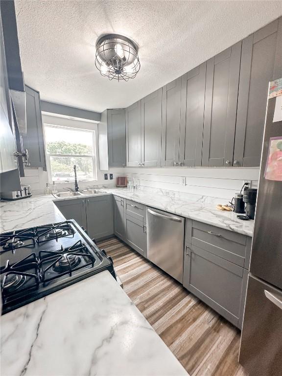 kitchen featuring stainless steel appliances, light stone countertops, sink, and gray cabinetry