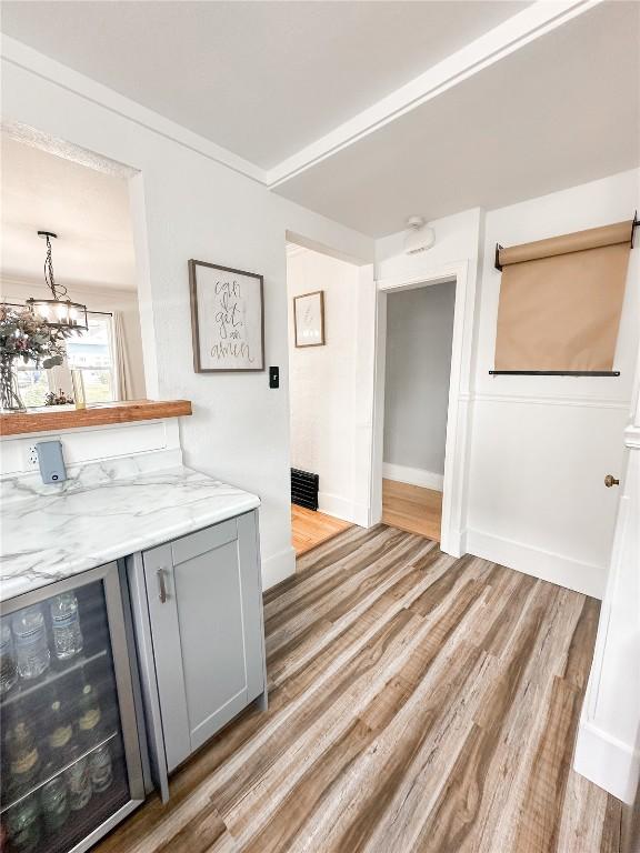 bar with wine cooler, gray cabinets, light hardwood / wood-style floors, and light stone countertops