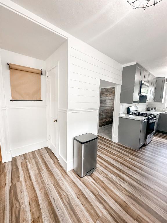 kitchen with stainless steel appliances, wooden walls, gray cabinets, and light hardwood / wood-style flooring