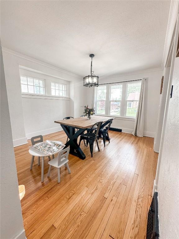 dining room with ornamental molding, a textured ceiling, light hardwood / wood-style flooring, and a notable chandelier