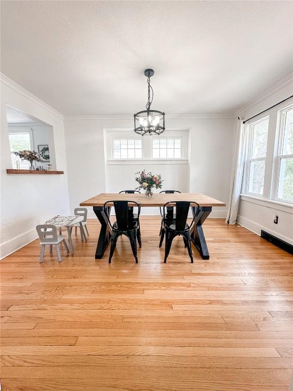 dining space with ornamental molding, a healthy amount of sunlight, an inviting chandelier, and light wood-type flooring