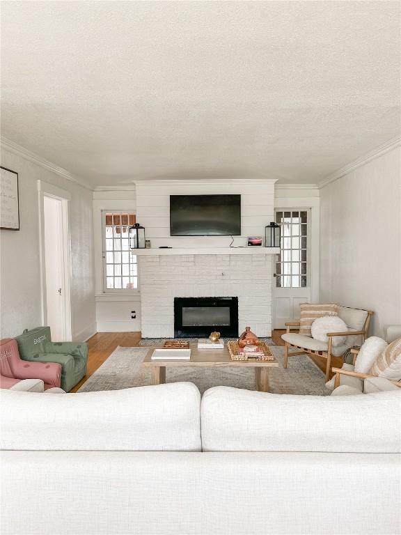 living room with a brick fireplace, wood-type flooring, ornamental molding, and a textured ceiling