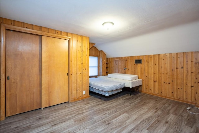 unfurnished bedroom featuring a closet, wood-type flooring, wood walls, and vaulted ceiling