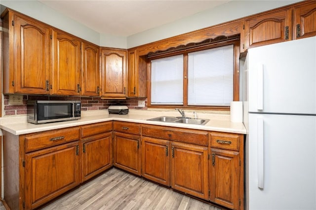 kitchen featuring white refrigerator, sink, light wood-type flooring, and decorative backsplash