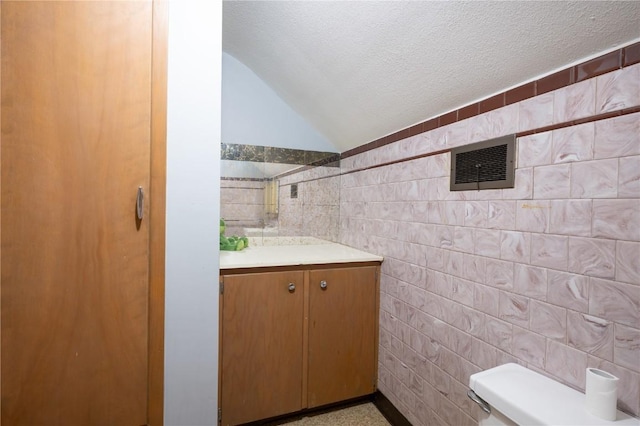 bathroom with vaulted ceiling, tile walls, vanity, toilet, and a textured ceiling