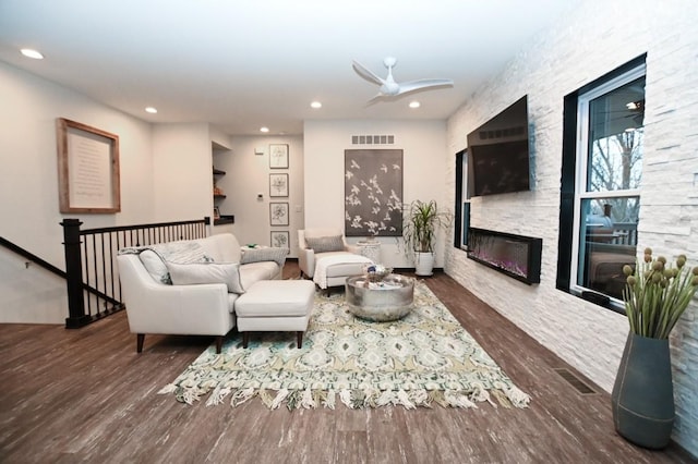 living room featuring dark hardwood / wood-style flooring, a stone fireplace, and ceiling fan