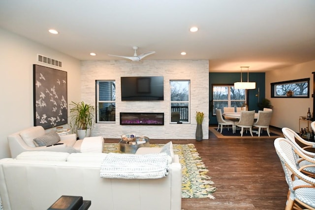 living room with dark wood-type flooring, a large fireplace, and ceiling fan