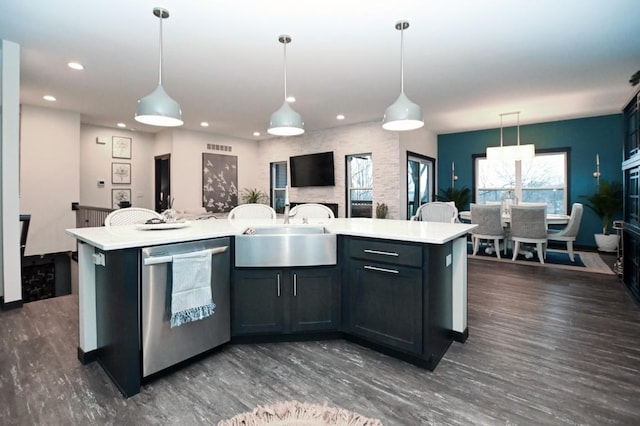 kitchen featuring stainless steel dishwasher, sink, decorative light fixtures, and an island with sink