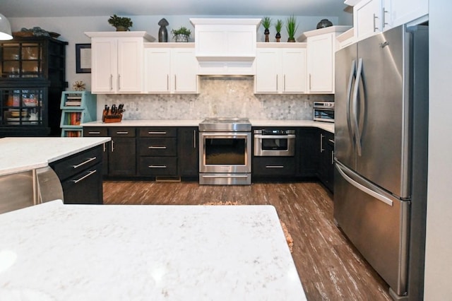 kitchen with appliances with stainless steel finishes, white cabinetry, dark hardwood / wood-style flooring, decorative backsplash, and custom range hood