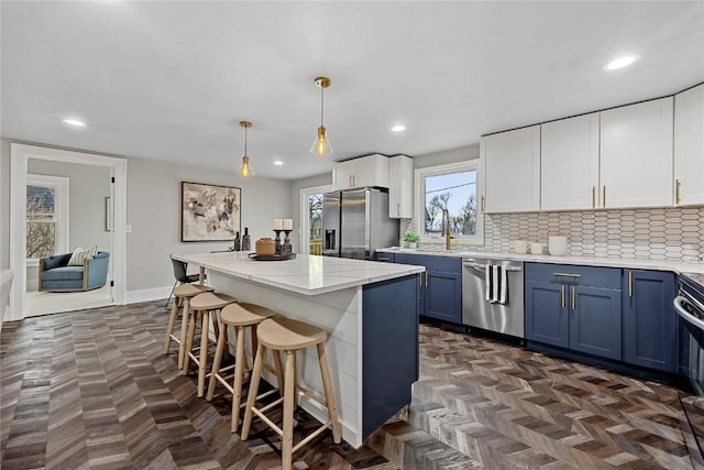 kitchen with a kitchen island, appliances with stainless steel finishes, decorative light fixtures, blue cabinets, and white cabinets