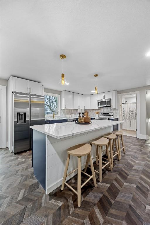 kitchen featuring stainless steel appliances, hanging light fixtures, white cabinets, and backsplash