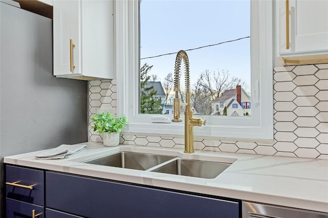 kitchen with tasteful backsplash, blue cabinets, sink, white cabinets, and light stone counters