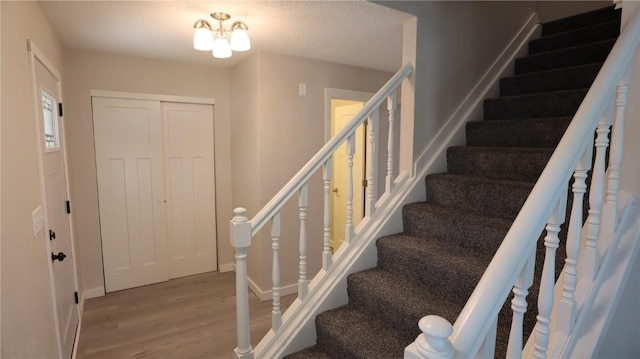 stairway featuring wood-type flooring, a chandelier, and a textured ceiling