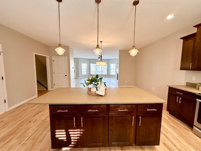 kitchen featuring pendant lighting, stainless steel stove, a kitchen island, and light hardwood / wood-style flooring