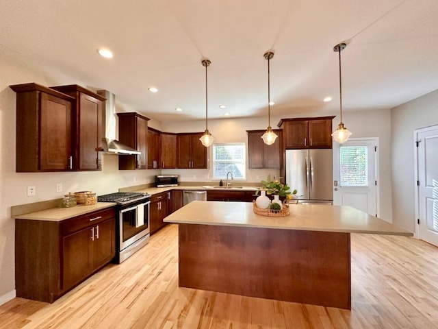 kitchen with wall chimney exhaust hood, stainless steel appliances, a center island, and hanging light fixtures