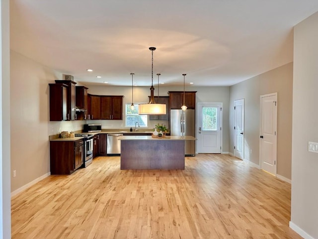 kitchen with sink, a center island, light wood-type flooring, pendant lighting, and stainless steel appliances