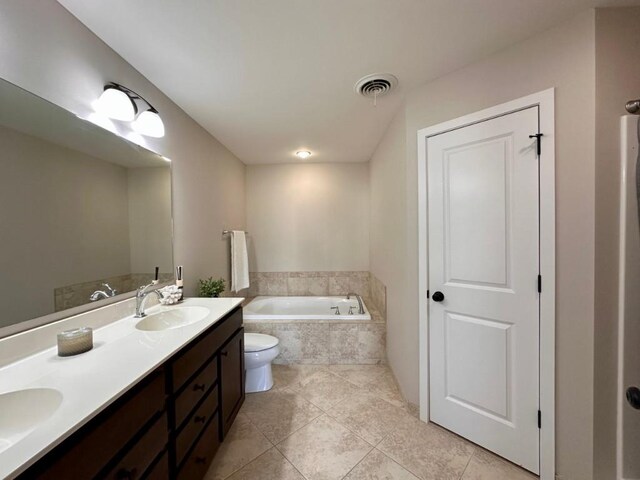 bathroom featuring a relaxing tiled tub, vanity, tile patterned flooring, and toilet