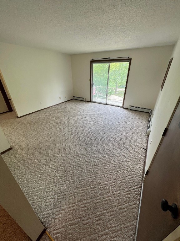 carpeted spare room featuring a baseboard radiator and a textured ceiling