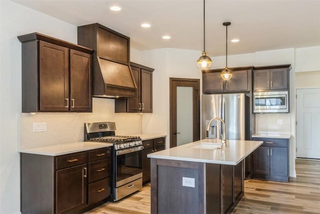 kitchen featuring appliances with stainless steel finishes, decorative light fixtures, an island with sink, sink, and custom exhaust hood