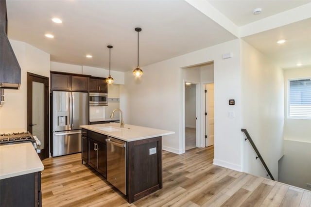 kitchen featuring appliances with stainless steel finishes, decorative light fixtures, sink, a center island with sink, and light hardwood / wood-style flooring