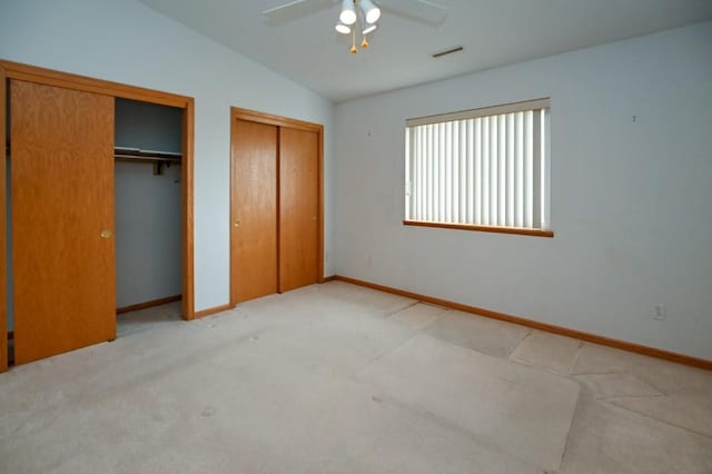 unfurnished bedroom featuring multiple closets, vaulted ceiling, light carpet, and ceiling fan