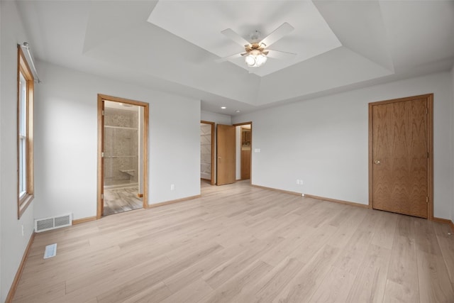 unfurnished bedroom with ceiling fan, connected bathroom, light wood-type flooring, and a tray ceiling