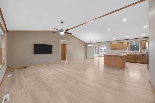 unfurnished living room featuring sink, ceiling fan with notable chandelier, vaulted ceiling, and light hardwood / wood-style floors