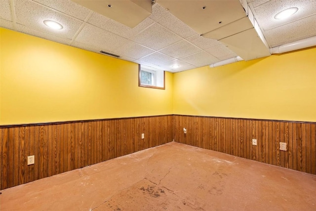 basement featuring wooden walls and a paneled ceiling