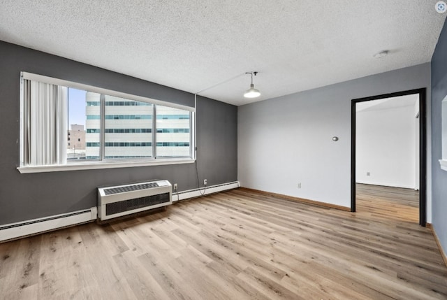 empty room featuring wood finished floors, baseboard heating, an AC wall unit, baseboards, and a textured ceiling