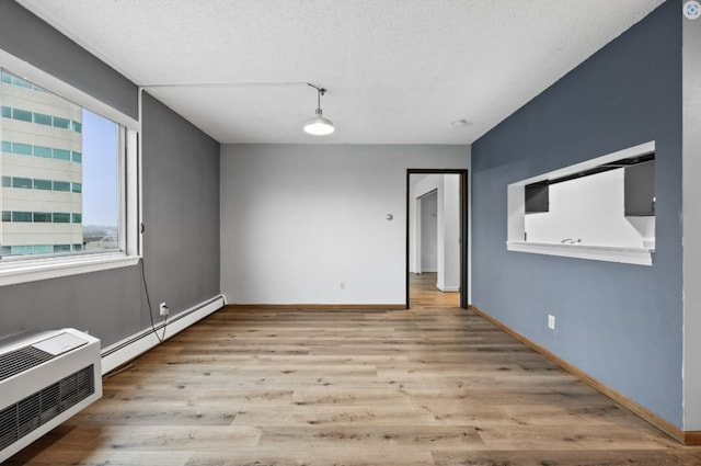 unfurnished dining area with a baseboard heating unit, a wall mounted air conditioner, baseboards, a textured ceiling, and wood finished floors