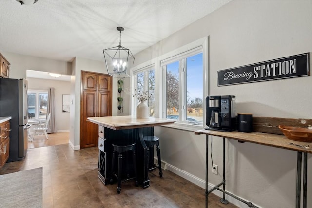 kitchen featuring a breakfast bar area, an inviting chandelier, a textured ceiling, stainless steel refrigerator, and pendant lighting