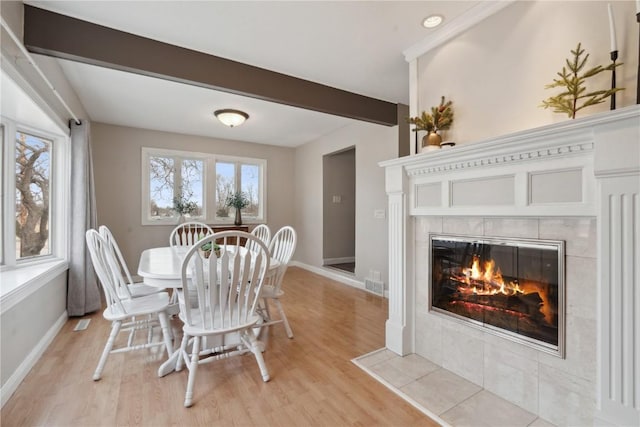 dining area with a fireplace, beam ceiling, and light hardwood / wood-style flooring