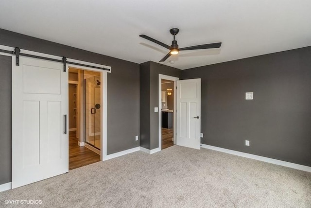 unfurnished bedroom featuring ensuite bathroom, a barn door, carpet floors, and ceiling fan