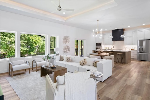 living room with a tray ceiling, ceiling fan with notable chandelier, and light hardwood / wood-style flooring