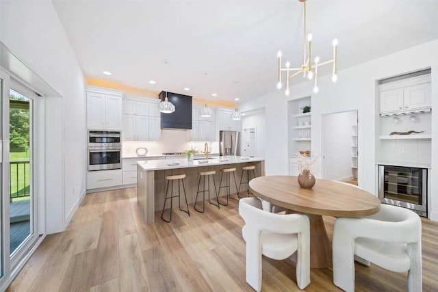 dining area with built in features, sink, wine cooler, an inviting chandelier, and light hardwood / wood-style flooring