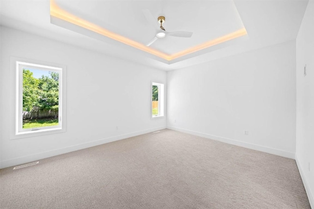 spare room with ceiling fan, carpet flooring, and a tray ceiling