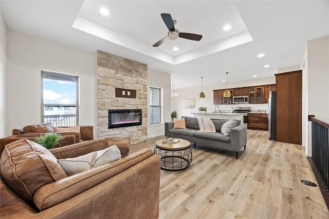 living room featuring ceiling fan, a fireplace, a tray ceiling, and light hardwood / wood-style floors