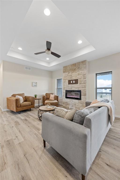 living room with a raised ceiling, ceiling fan, a fireplace, and light hardwood / wood-style floors