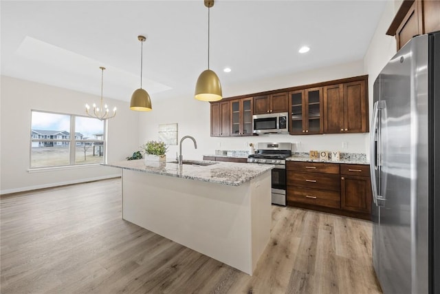 kitchen with sink, hanging light fixtures, appliances with stainless steel finishes, an island with sink, and light stone countertops